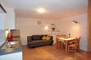 A compact living space with a kitchenette, a sofa, a dining table, and a clock on the wall.
