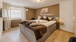 Ein Schlafzimmer mit Bett, Nachttisch, Lampe, Stuhl, einem Fenster mit Vorhängen und einem Gemälde an der Wand.
