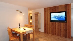 Ein Essbereich mit Holztisch und -stühlen, einem an einer Holzwand montierten Fernseher und einer Tür zu einem anderen Raum.