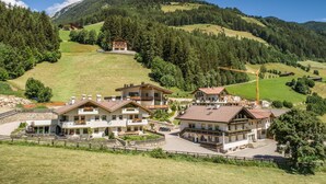 Ein Bergresort mit mehreren Chaletbauten, einer gepflasterten Auffahrt und Blick auf die umliegenden bewaldeten Hügel.