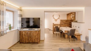 Ein modernes Wohnzimmer mit einer Holzeinbauwand, einem Essbereich mit Holztisch und -stühlen sowie einem großen, an der Wand befestigten Fernseher.