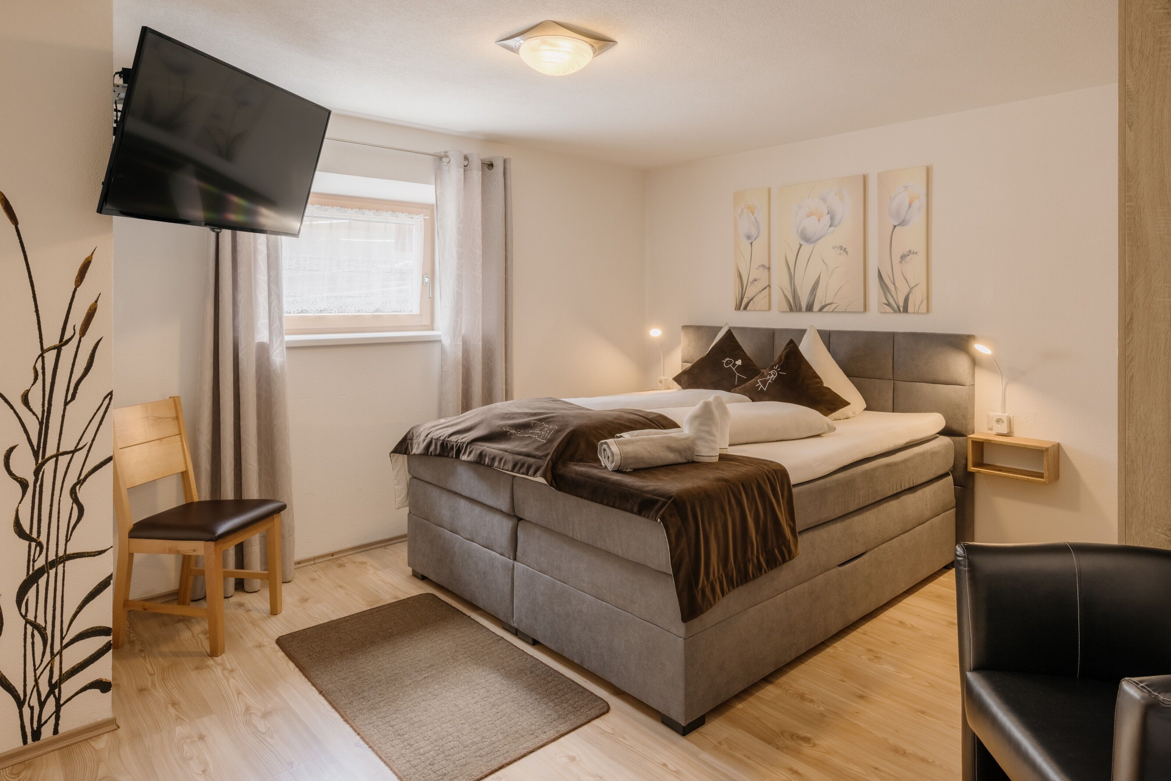 A bedroom with a bed, a TV, a chair, and a window.
