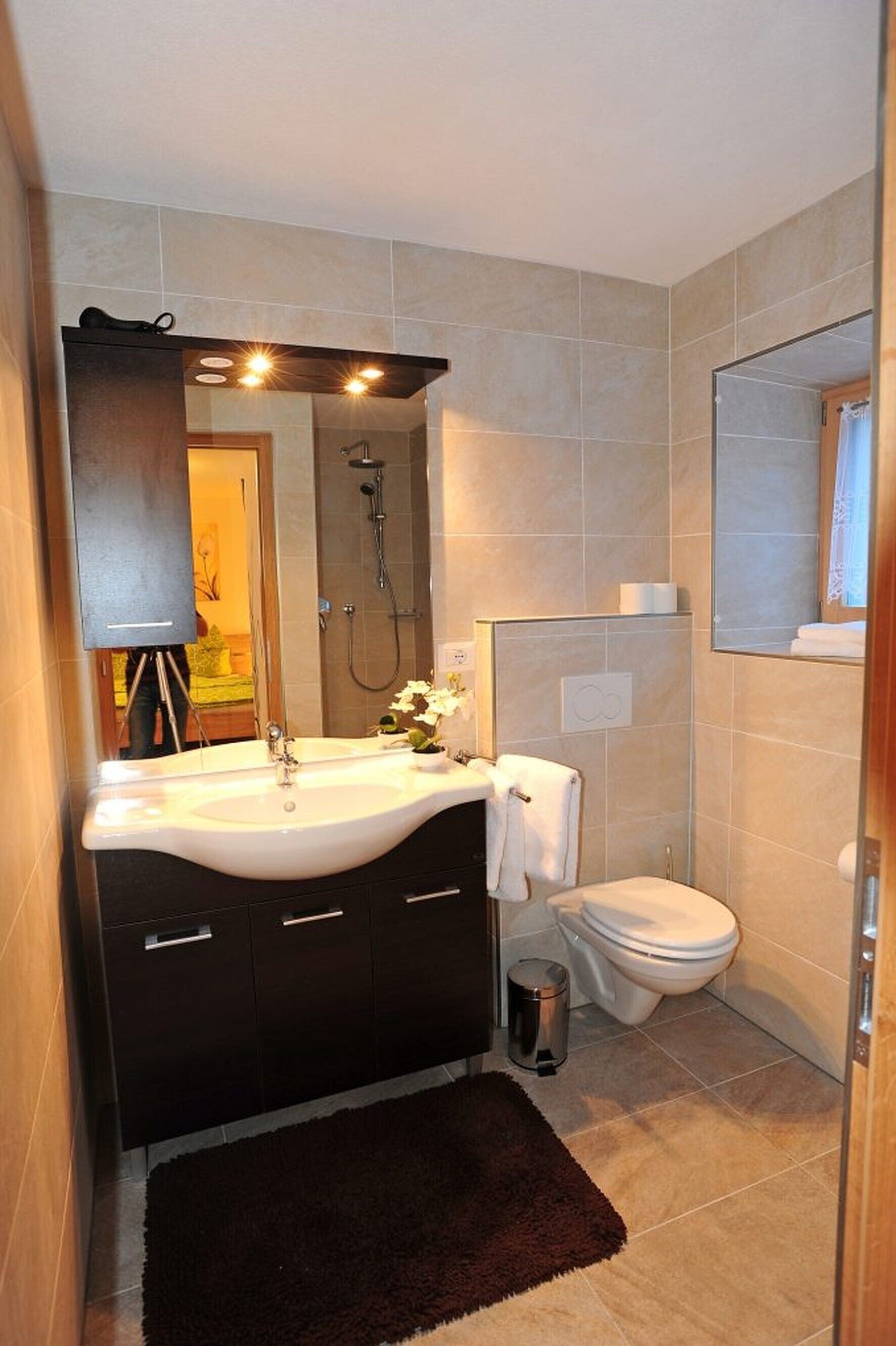 A bathroom with a sink, mirror, shower, toilet, and a dark rug on the floor.