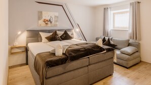 Ein Schlafzimmer mit Bett, Sofa, Nachttisch, Lampe, Gemälde und einem Fenster mit Vorhängen.