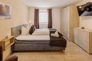 Een slaapkamer met een bed, een televisie, een raam met gordijnen, een nachtkastje en een houten garderobe.