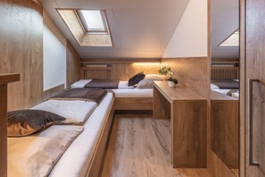 Une chambre de taille modeste, avec deux lits, un petit bureau et une fenêtre de toit.