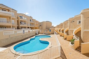 A swimming pool surrounded by beige buildings with balconies and a clear sky.