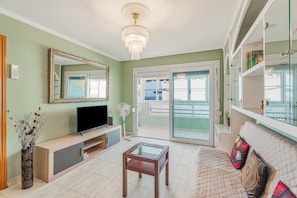 A living room with a television, a glass coffee table, a sofa, a mirror, and a balcony with a view.