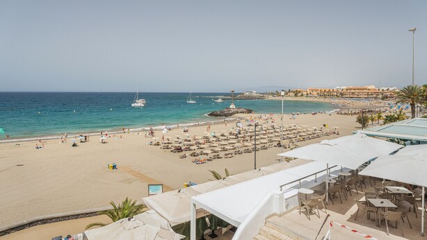 A beach with umbrellas, lounge chairs, and a view of the sea and boats. - Vacation Apartment 'Ceyla 214' with Sea View, Private Terrace and Wi-Fi (Arona)