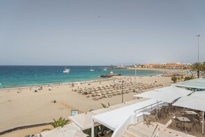 A beach with umbrellas, lounge chairs, and a view of the sea and boats. - Vacation Apartment 'Ceyla 214' with Sea View, Private Terrace and Wi-Fi (Arona)
