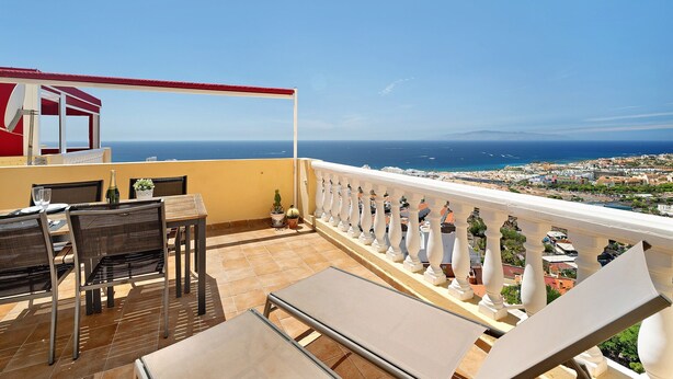 Ein Balkon mit Tisch, Stühlen und Blick auf das Meer und die Stadt.