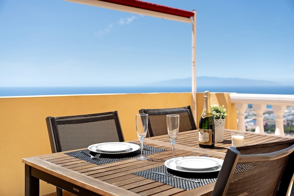 A table set for two with a bottle of champagne, two glasses, and a candle on a balcony with a clear view of the sea.