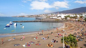 A beach with people sunbathing, umbrellas, and boats. - Vacation Home "Club Atlantis 223" with Sea View, Shared Pool & Wi-Fi (Adeje)