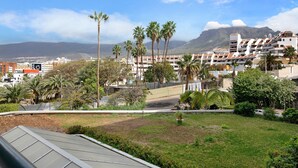 A residential area with a view of mountains, palm trees, and a building with balconies. - Vacation Home "Club Atlantis 223" with Sea View, Shared Pool & Wi-Fi (Adeje)