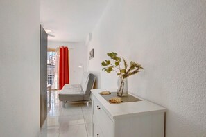 A hotel room with a bed, a white dresser, a vase with dried plants, and a window with red curtains. - Holiday Apartment 'Los Geranios 304' with Shared Pool, Private Terrace and Wi-Fi (Adeje)