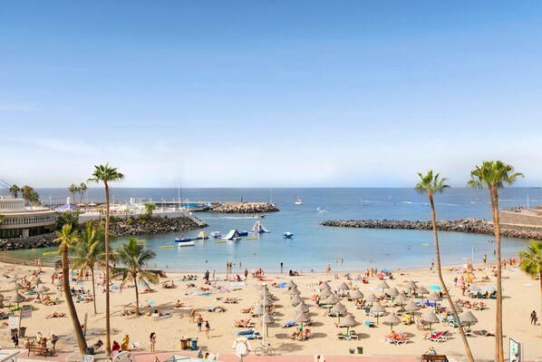A beach with palm trees, umbrellas, and people.