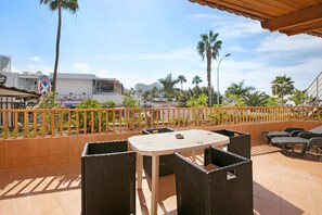 A terrace with wicker furniture, a table, and a view of palm trees and buildings. - Holiday Apartment 'Los Geranios 304' with Shared Pool, Private Terrace and Wi-Fi (Adeje)