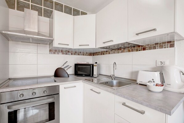 Una cocina moderna con gabinetes blancos, una estufa de acero inoxidable, un microondas, un tostador y una cafetera.