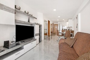 Una sala de estar moderna con un televisor de pantalla plana, un sofá y un comedor con sillas y una mesa.