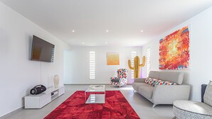 Un salon moderne avec un tapis rouge, un téléviseur à écran plat, un canapé et un fauteuil coloré.