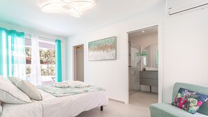 Une chambre à coucher avec un lit, un canapé, un tableau et une salle de bain visible à travers une porte ouverte.