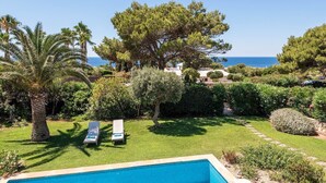 Una piscina con dos tumbonas, una palmera y vistas al mar.