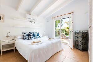 Ein Schlafzimmer mit einem Bett, Nachttischen, einer Klimaanlage, einem Fenster und Blick ins Freie.