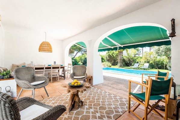 Eine Terrasse mit Esstisch, Stühlen, einer Hängeleuchte und Blick auf einen Swimmingpool.