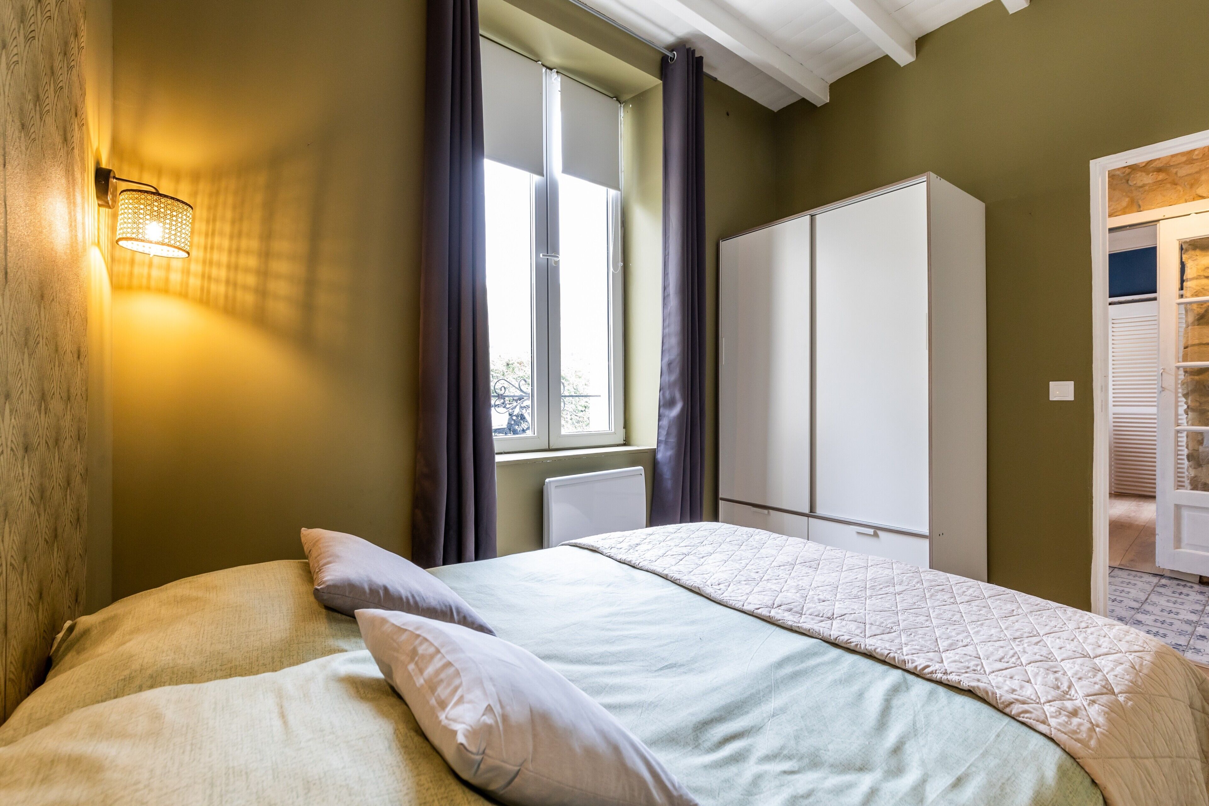 A bedroom with a bed, a wardrobe, and a window with curtains.