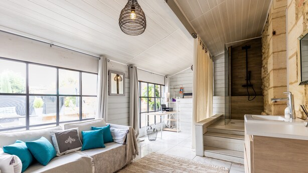 Una habitación con techo de madera, un banco empotrado con cojines, un ventanal grande y una zona de ducha.