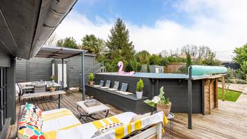 An outdoor deck with a pool table, seating area, and a hot tub.