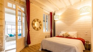Una habitación con cama, cortina roja, suelo de madera, espejo circular y ventana.