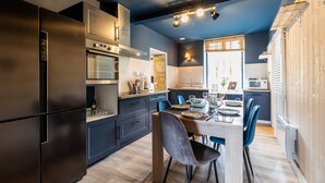 Una cocina moderna con armarios oscuros, un refrigerador de acero inoxidable y un comedor con mesa y sillas.