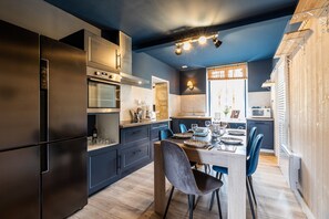 Une cuisine moderne avec des meubles de couleur sombre, un réfrigérateur en acier inoxydable et un coin repas comprenant une table et des chaises.