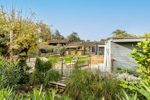 Un jardin avec une terrasse en bois, un petit abri de jardin et une maison avec un toit en tuiles.