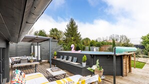 A deck with a sofa, a table, and a hot tub. - Stone House with Pool (vertheuil)