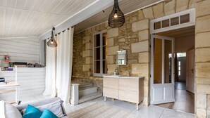A room with a stone wall, a wooden ceiling, a sofa with cushions, a white dresser, and a hanging light fixture. - Stone House with Pool (vertheuil)