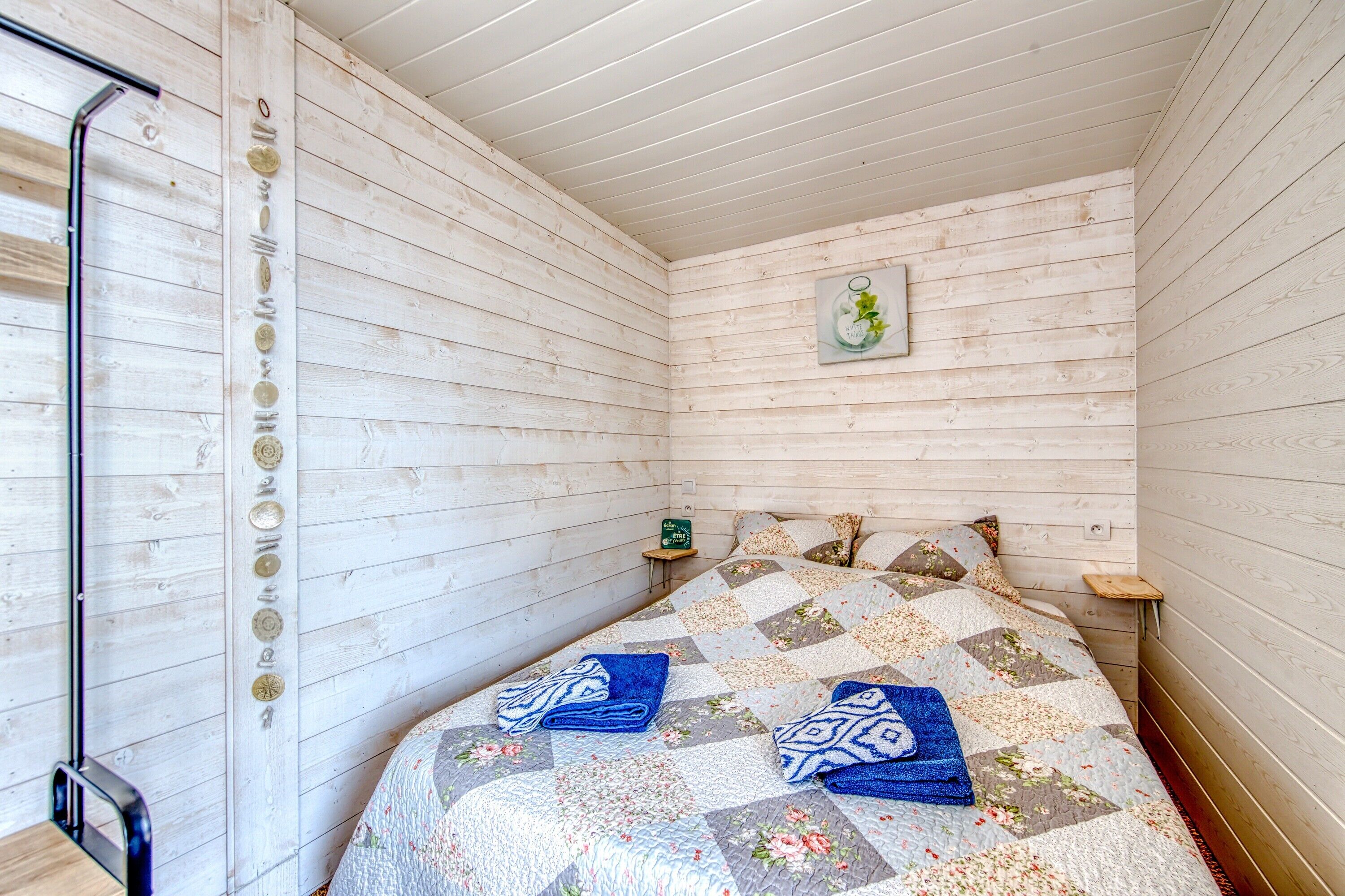 A wooden-paneled room with a bed, a small bedside table, and a wall-mounted picture.