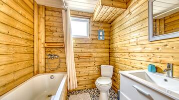 Een houten badkamertje in een chalet, met bad, toilet en wastafel.