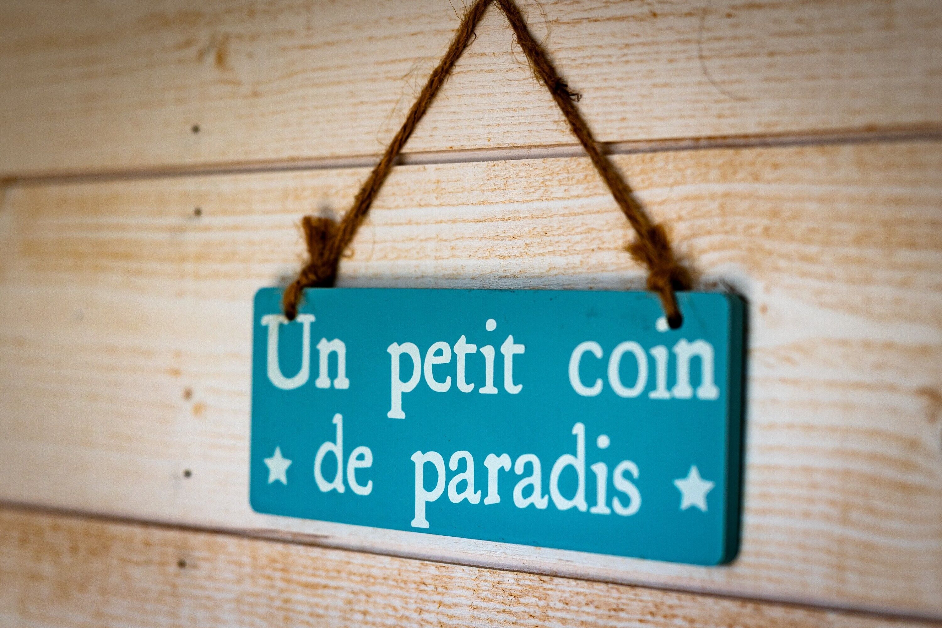 A sign with the text 'Un petit coin de paradis' hanging on a wooden wall.