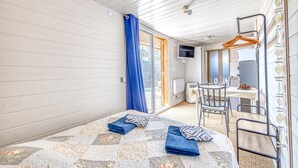 A room with a bed, a small table with chairs, a TV, and a window with curtains.