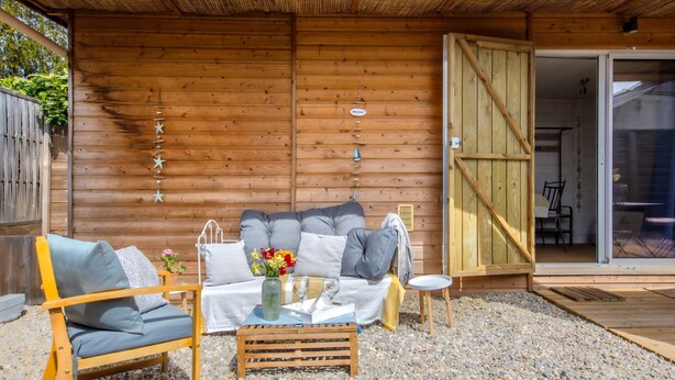 A wooden cabin with a sofa, chairs, and a small table with a vase and glass.