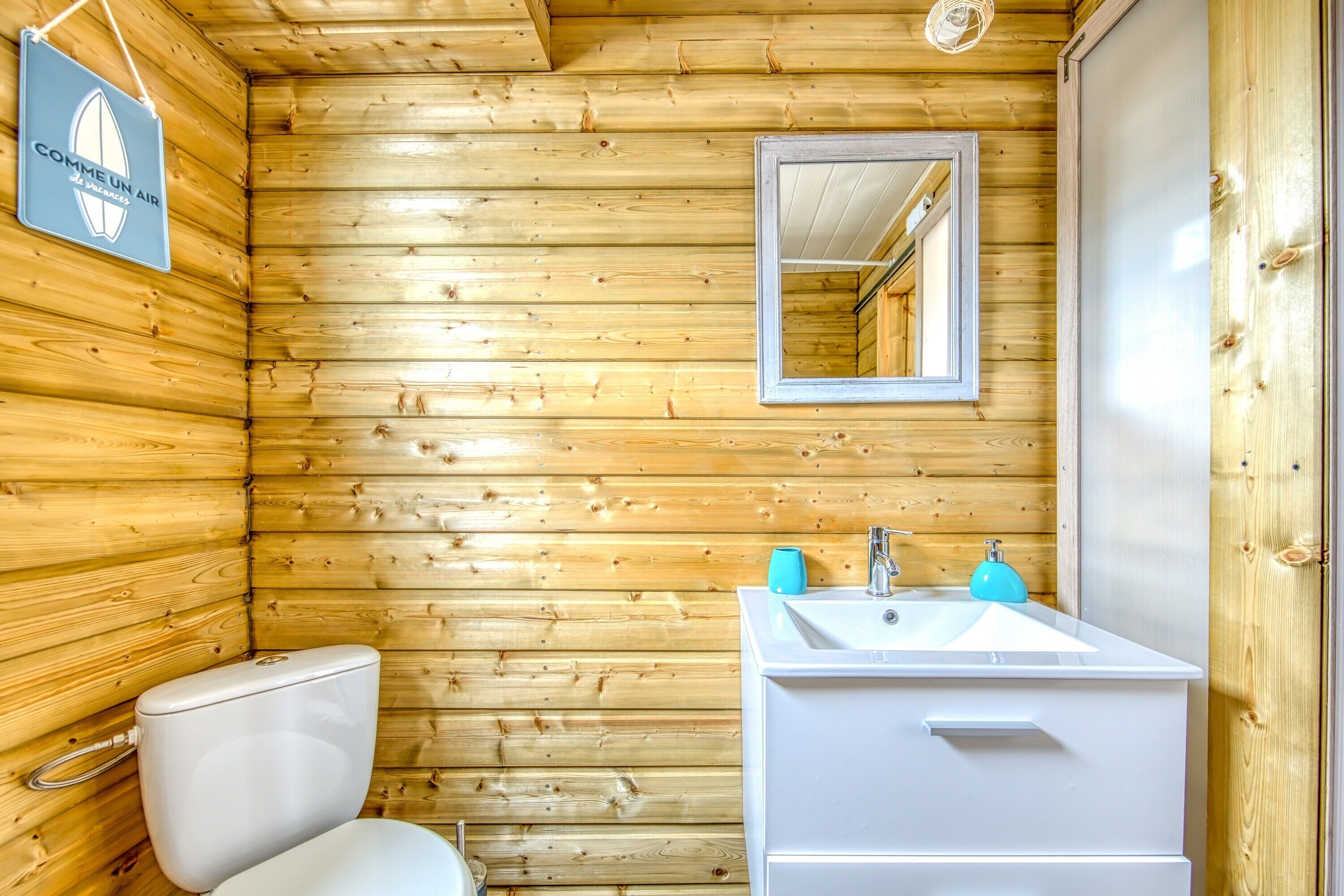 Une salle de bain rustique, aménagée dans une cabane en bois, avec des toilettes, un lavabo et un miroir.