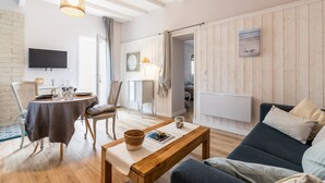Ein Wohnzimmer mit Sofa, Couchtisch, Wand-Fernseher und Essbereich mit Tisch und Stühlen.