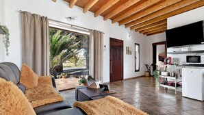 A living room with a sofa, a coffee table, a TV, and a kitchen area with a microwave. - Holiday Home 'Guenia I' with Mountain View, Wi-Fi and Air Conditioning (Teguise)