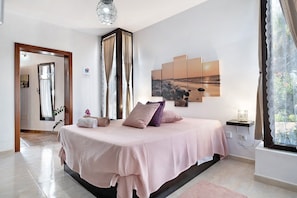 Une chambre à coucher avec un lit, une fenêtre avec des rideaux, une œuvre d’art accrochée au mur et une table de chevet.