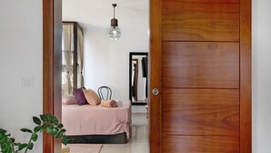 A bedroom with a bed, a hanging light fixture, a mirror, and a wooden door. - Holiday Home 'Guenia I' with Mountain View, Wi-Fi and Air Conditioning (Teguise)
