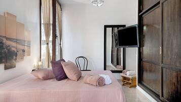 Une chambre à coucher avec un lit, des oreillers, une télévision, un miroir et une fenêtre avec des rideaux.