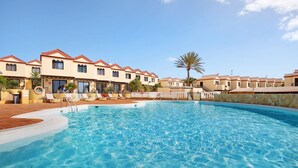A swimming pool with clear blue water, surrounded by buildings with red-tiled roofs and beige walls.