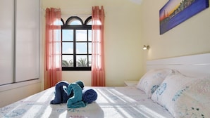 A bedroom with a bed, a window with curtains, and a painting on the wall.